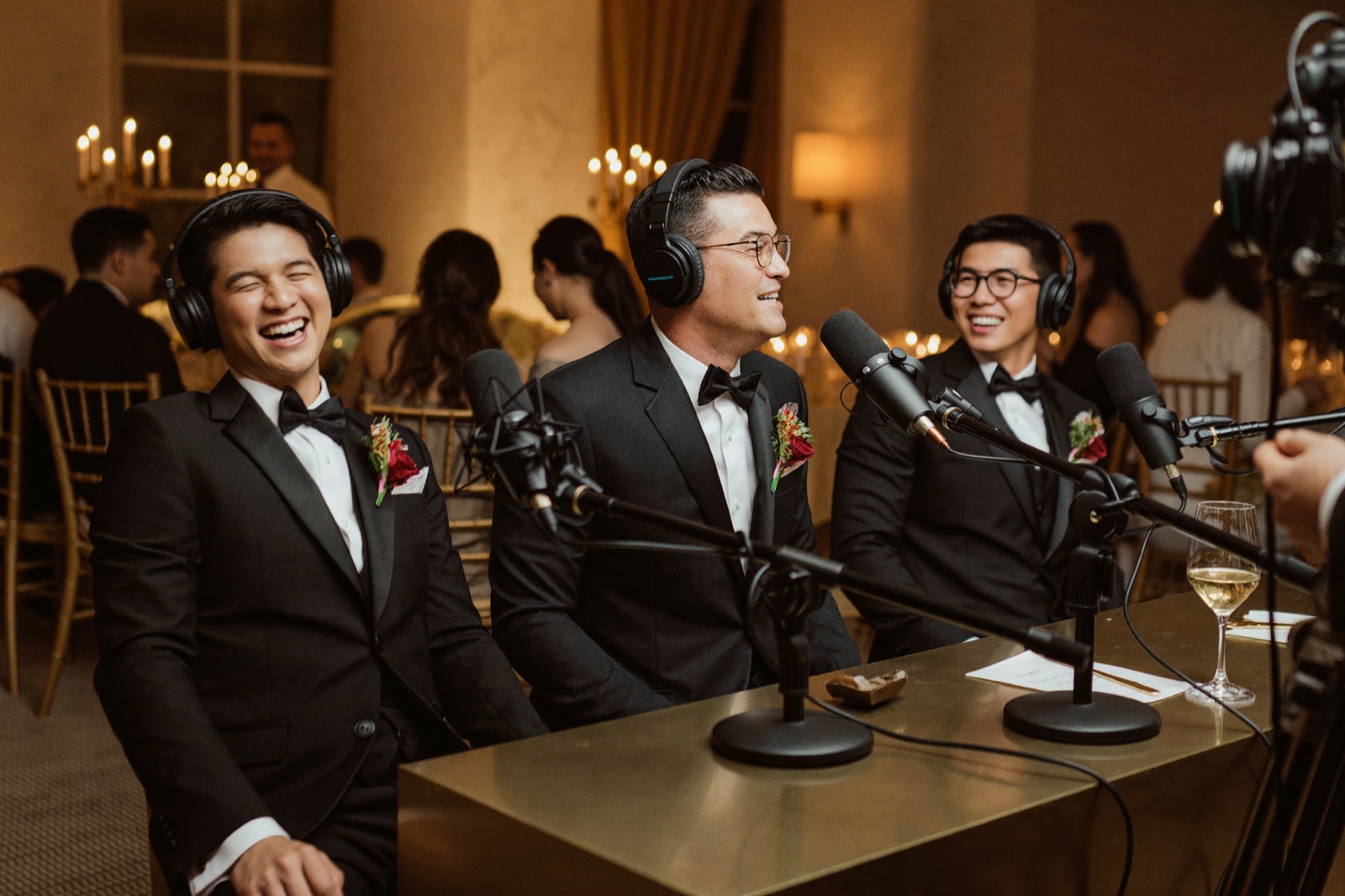 Groomsmen in tuxedos with headphones laughing around the podcast microphones